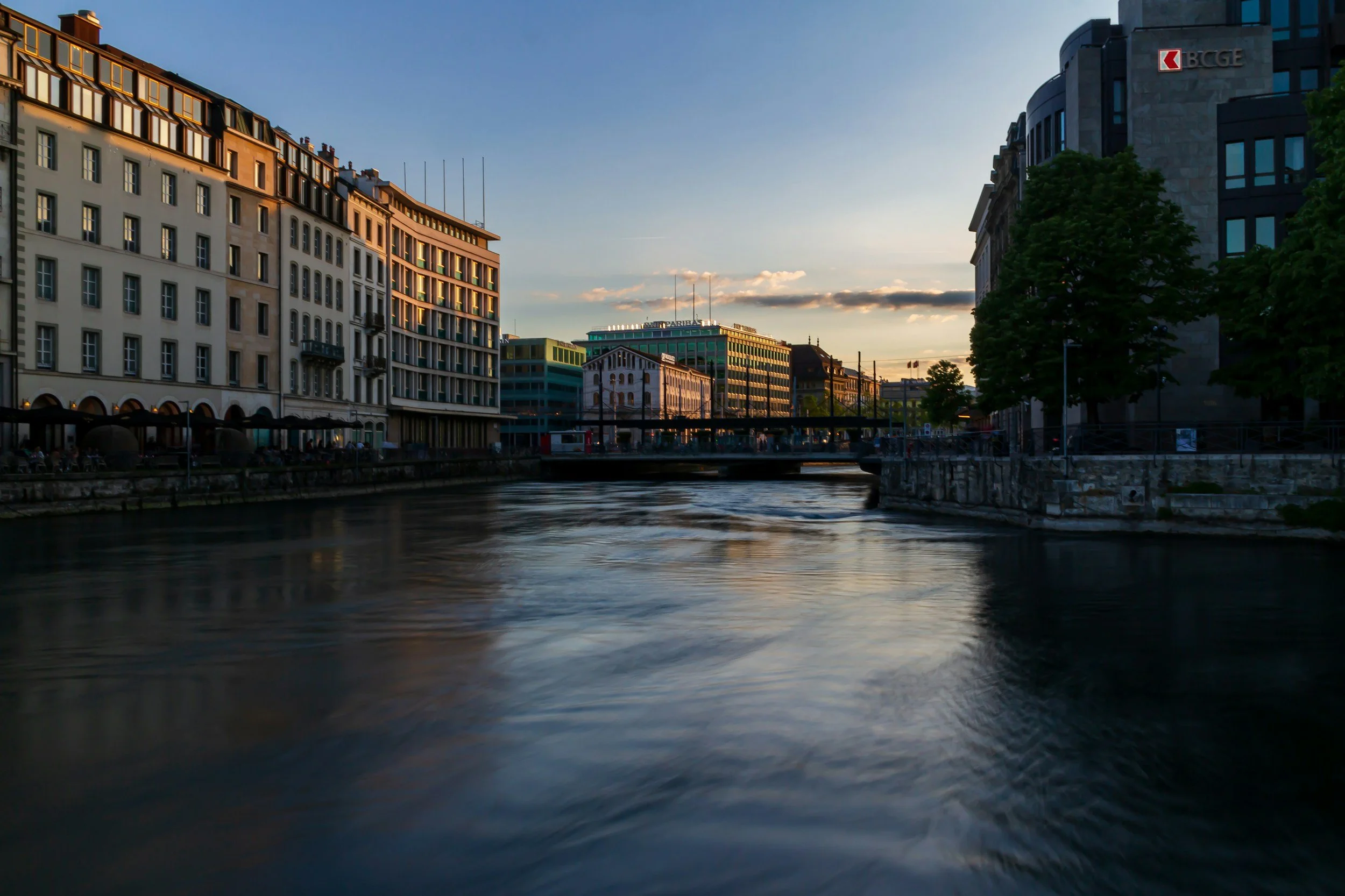 Coucher de soleil sur une ville avec des bâtiments modernes bordant une rivière.