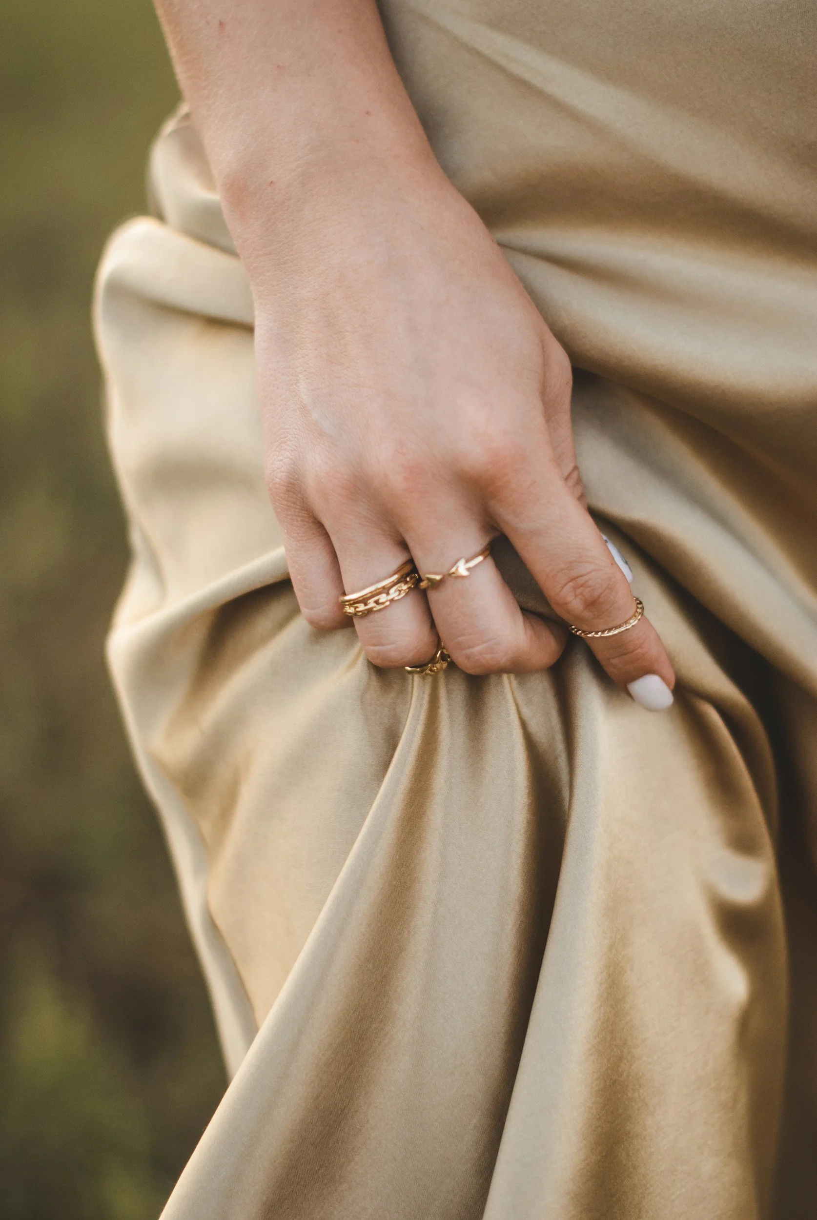 Close-up of a person's hand resting on beige fabric, wearing multiple gold rings.