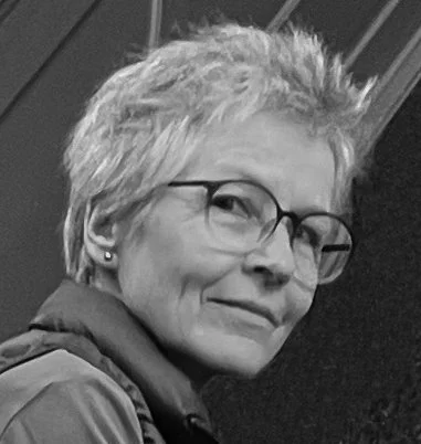 Schwarz-weiss-Foto der Künstlerin Judith Künzle mit Kurzhaarfrisur, Brille und freundlichem Gesichtsausdruck.