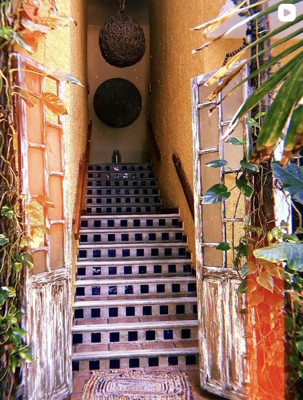 Outdoor staircase leading to an interior door, with plants on both sides, hanging decorative spheres at the top, and a doormat at the bottom of the stairs.