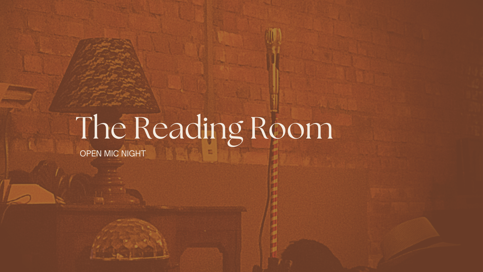 A cozy reading room with a brick wall, a table lamp with a patterned lampshade, and a vintage microphone standing on a striped stand, overlaid with text for an open mic night event.