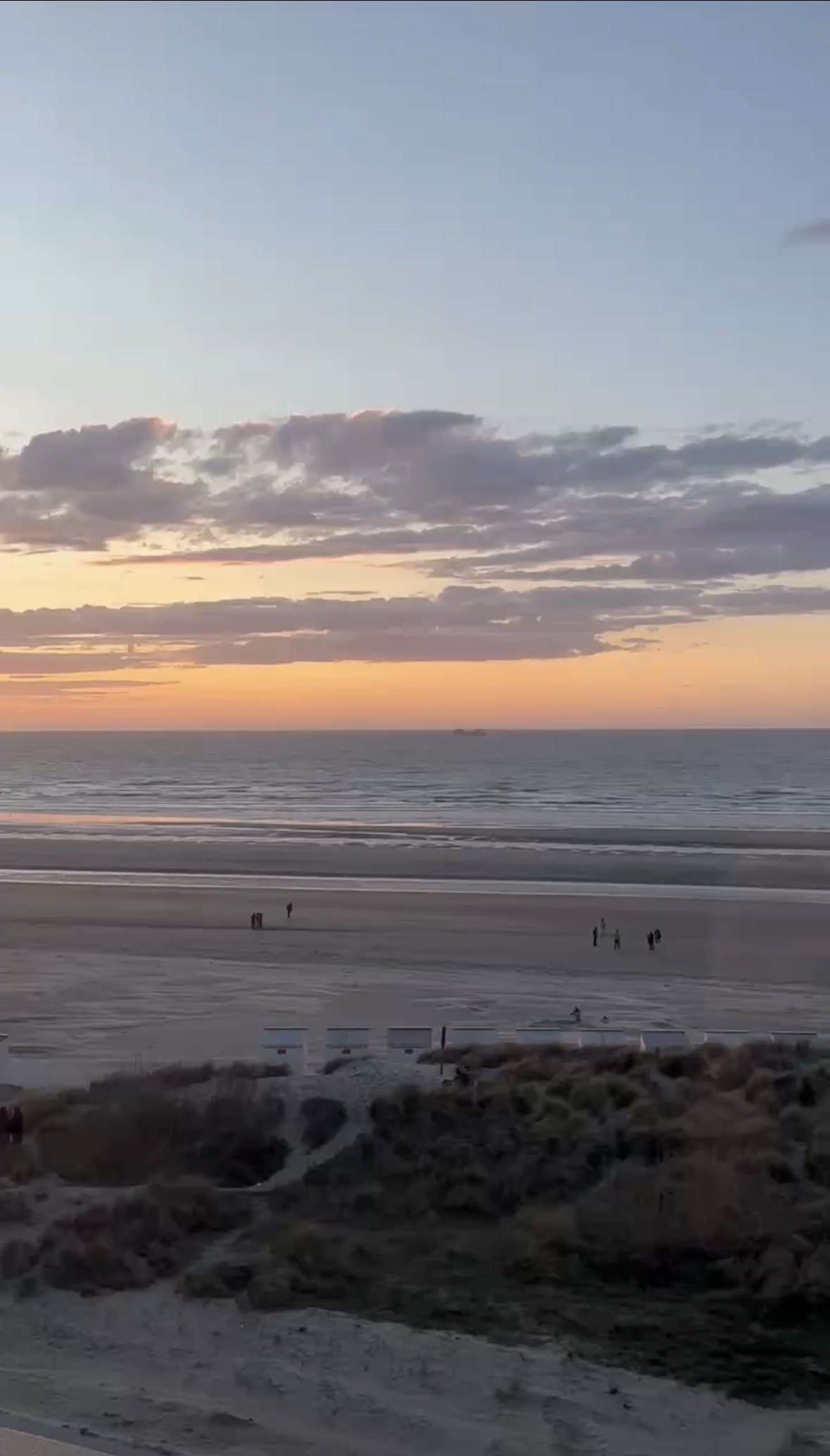 Sunset over the ocean with a few clouds in the sky and some people walking on the sandy beach.