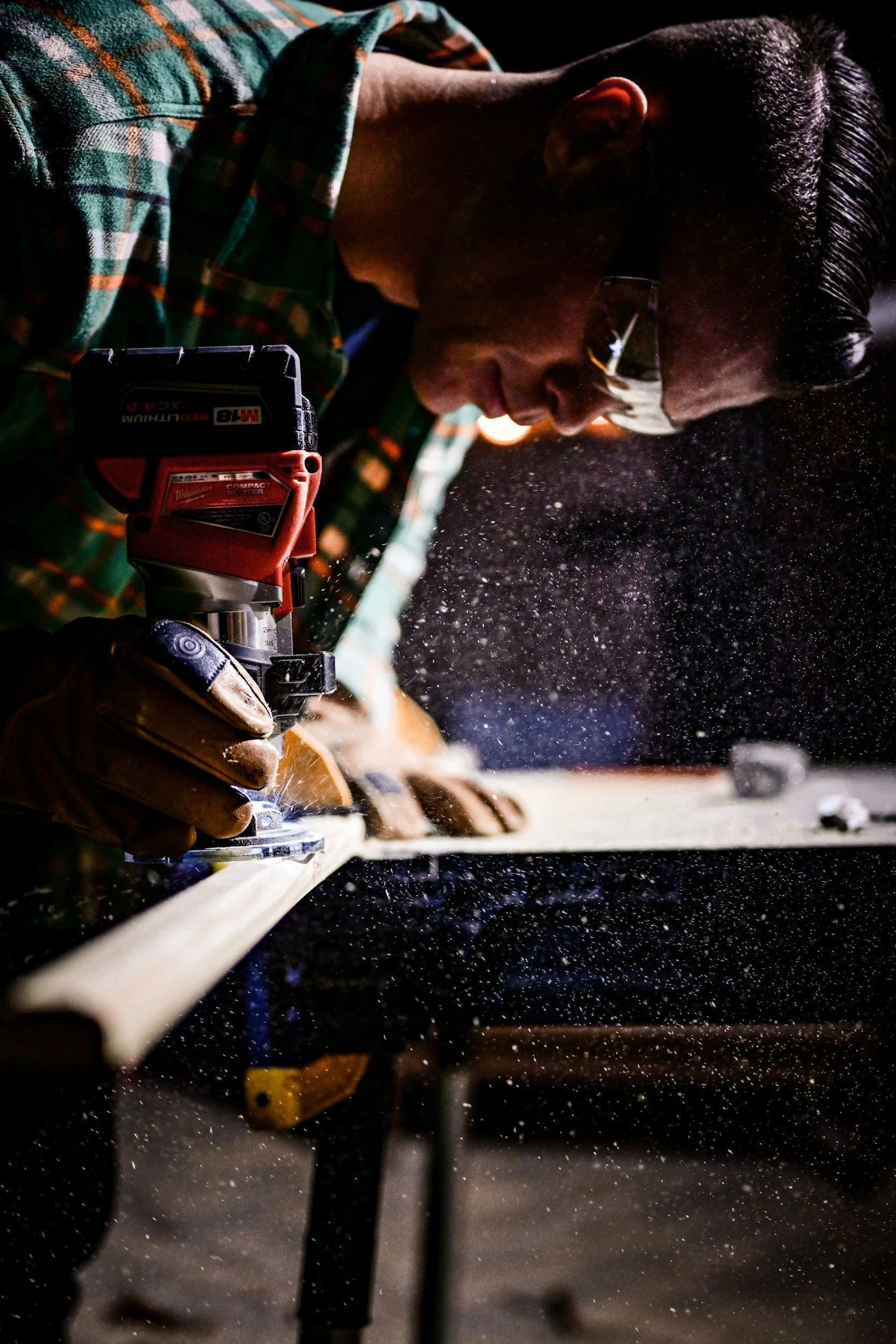 Handwerker schneidet mit einer elektrischen Stichsäge an einem Holzstück, bei Nacht, Staubpartikel in der Luft.
