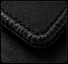 Close-up of a black woven or braided material, possibly part of a bag or accessory, on a dark background.