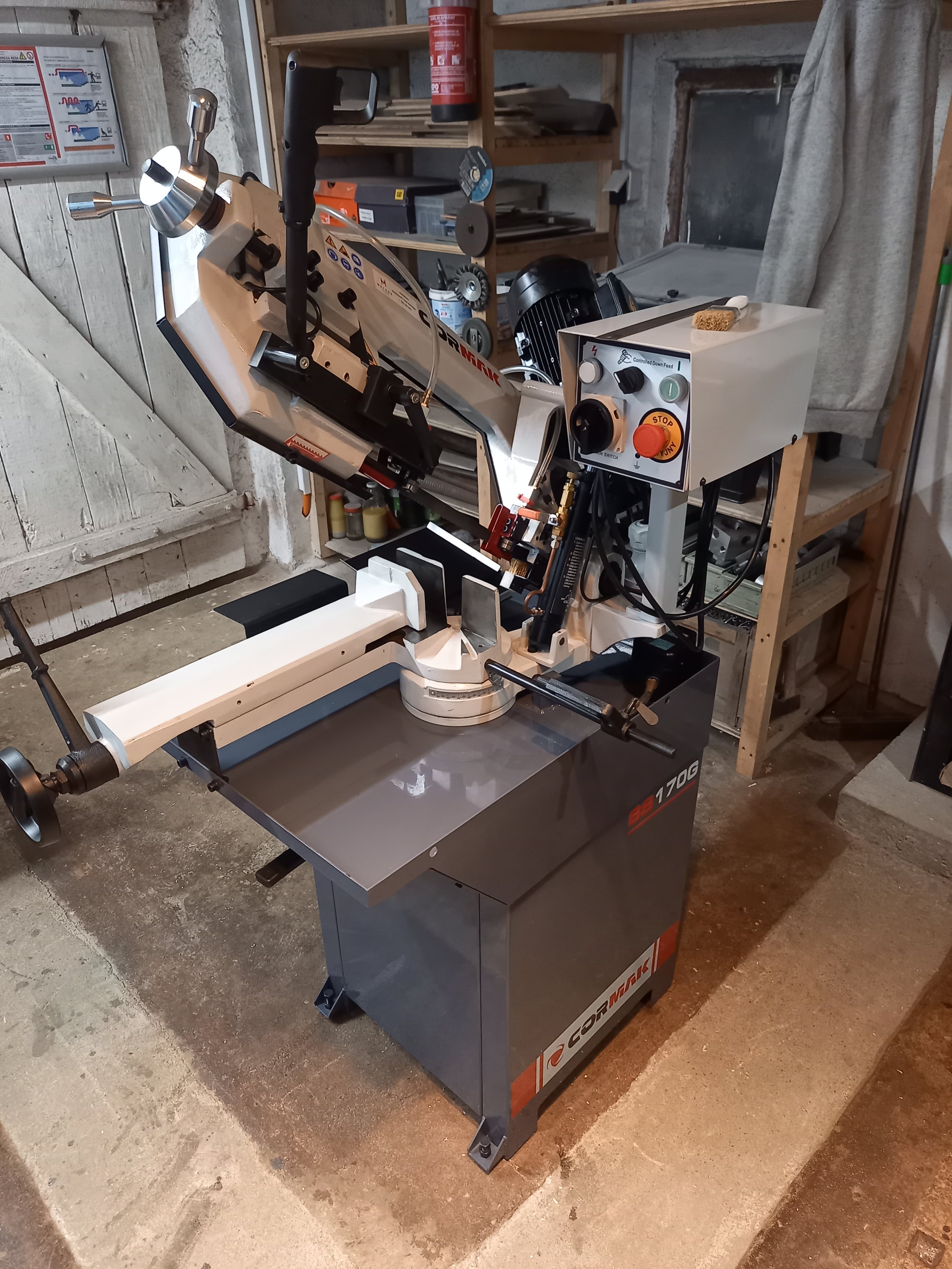 A band saw machine in a workshop with shelves and tools in the background.
