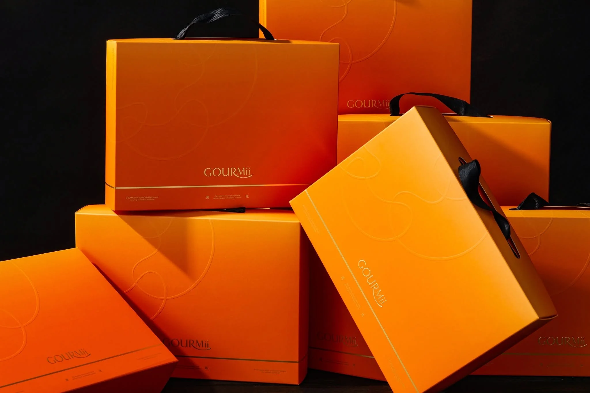 Several bright orange boxes with black handles, labeled "GOURMii," stacked against a black background.