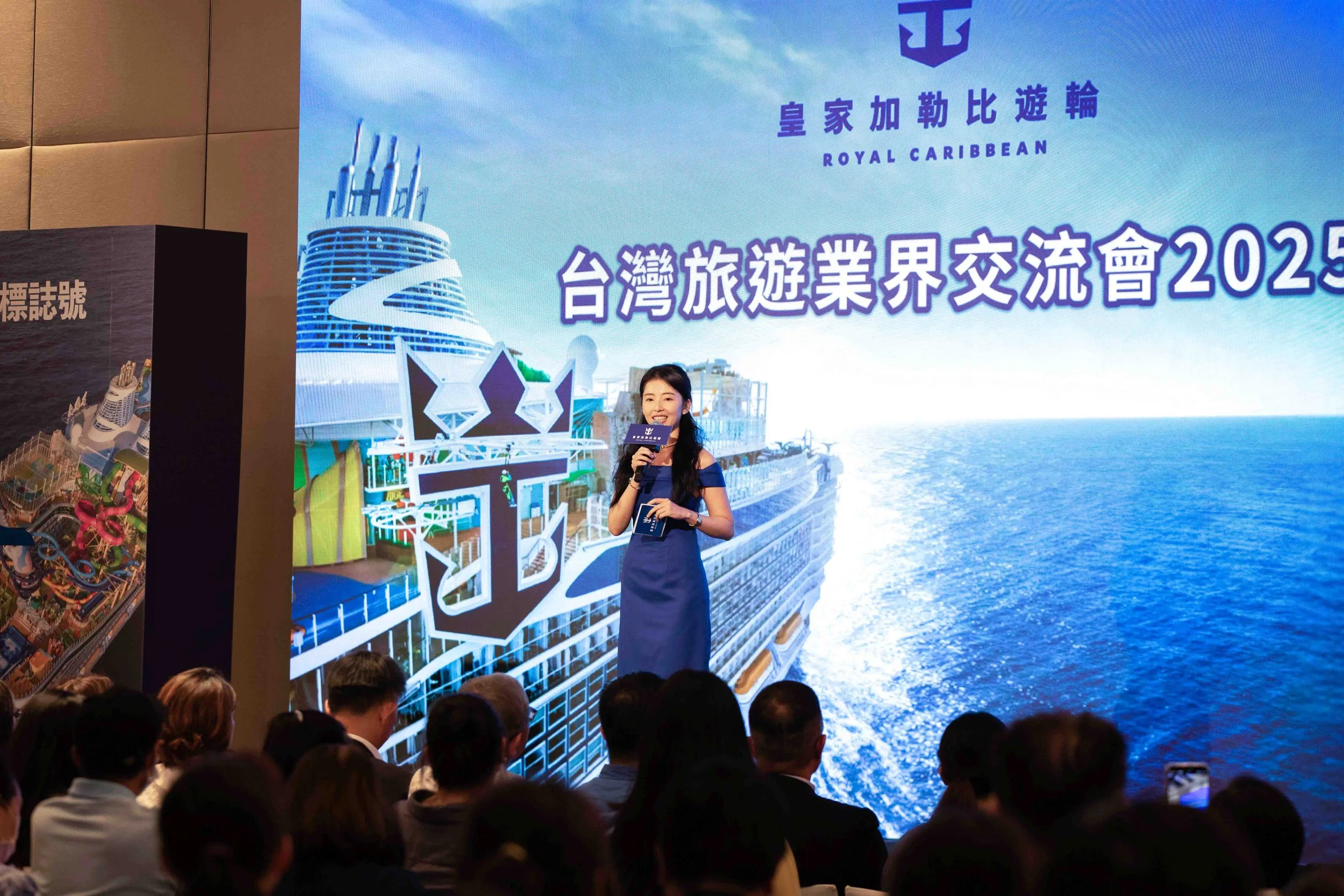 A woman in a blue dress speaking at a conference with a large digital screen behind her displaying a cruise ship and the text 'Royal Caribbean' and Chinese characters.