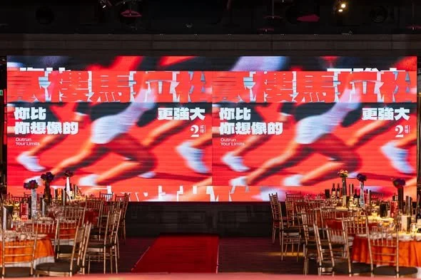 Large screen displaying red and white text in Chinese characters at a banquet hall with round tables and chairs, set for an event.