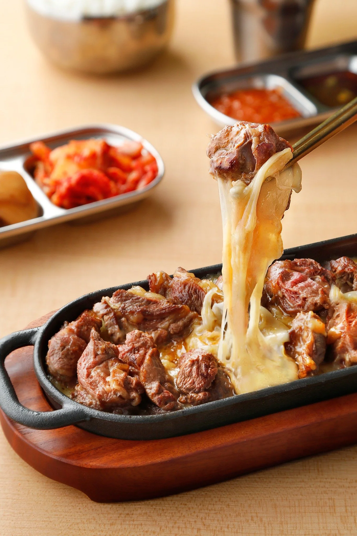 A cast iron skillet filled with cooked beef chunks topped with melted cheese, placed on a wooden serving board.