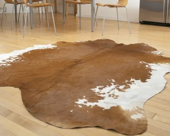 Cowhide rug on a wooden floor in a room with chairs and a kitchen area.