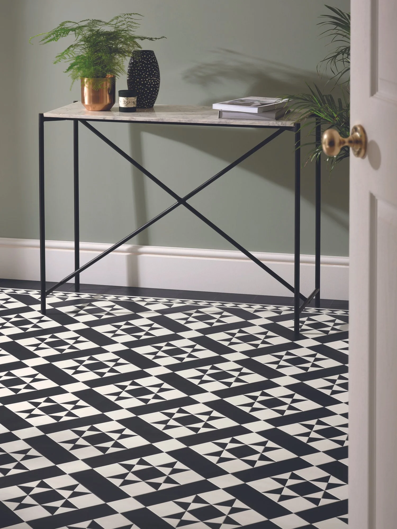 Parital view of a hallway with mosaic black and white tile effect on the floor. Console table against moss green wall in the background.