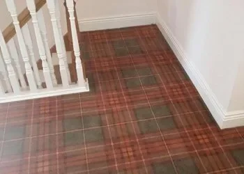 Flooring with a plaid carpet pattern near a staircase and white wall.