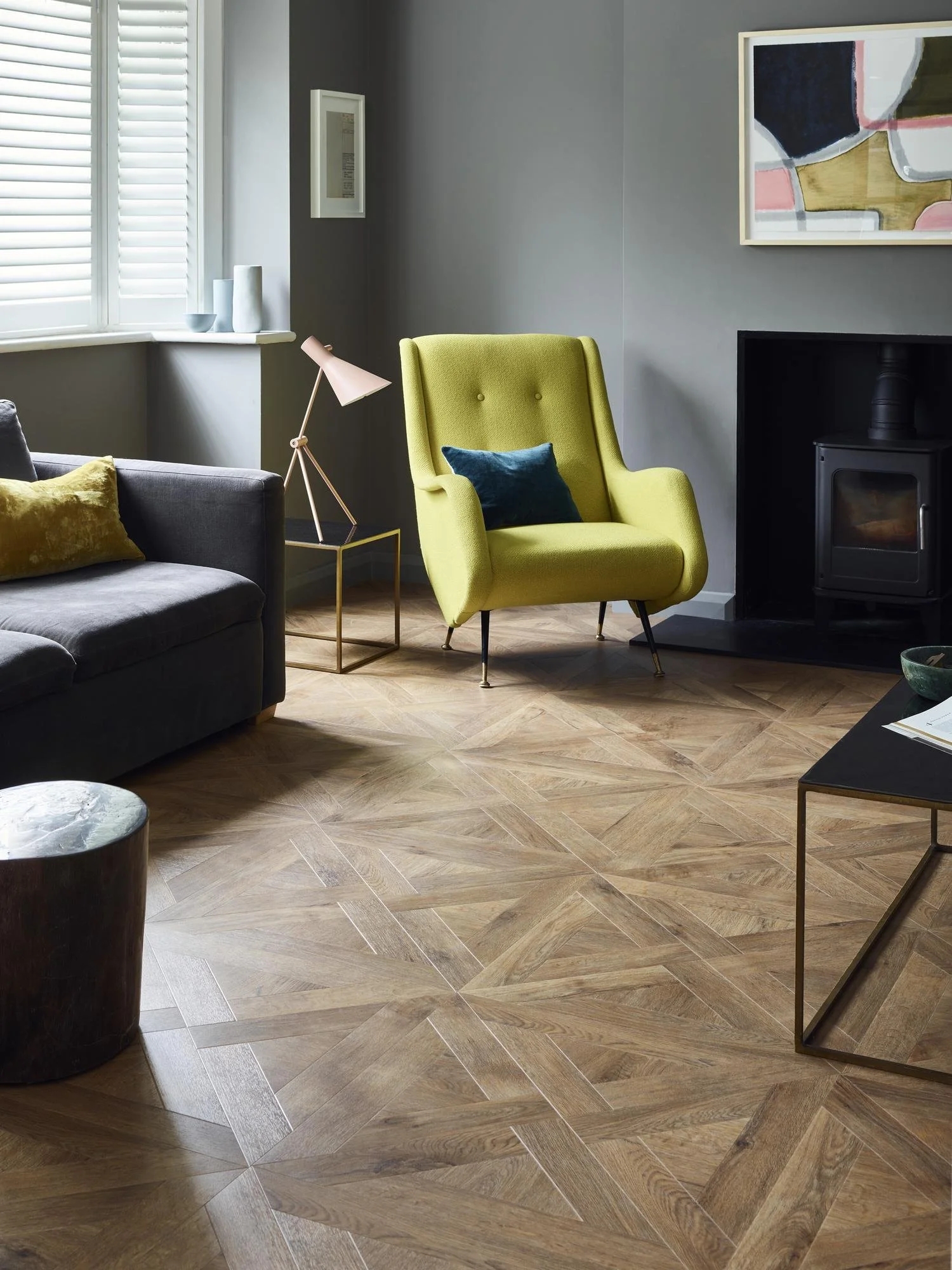 Stylish living room with grey furniture and walls, a single pale yellow armchair and a french weave parquet flooring in oak.