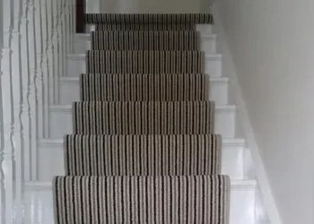 Indoor staircase with striped carpet runner and white walls.