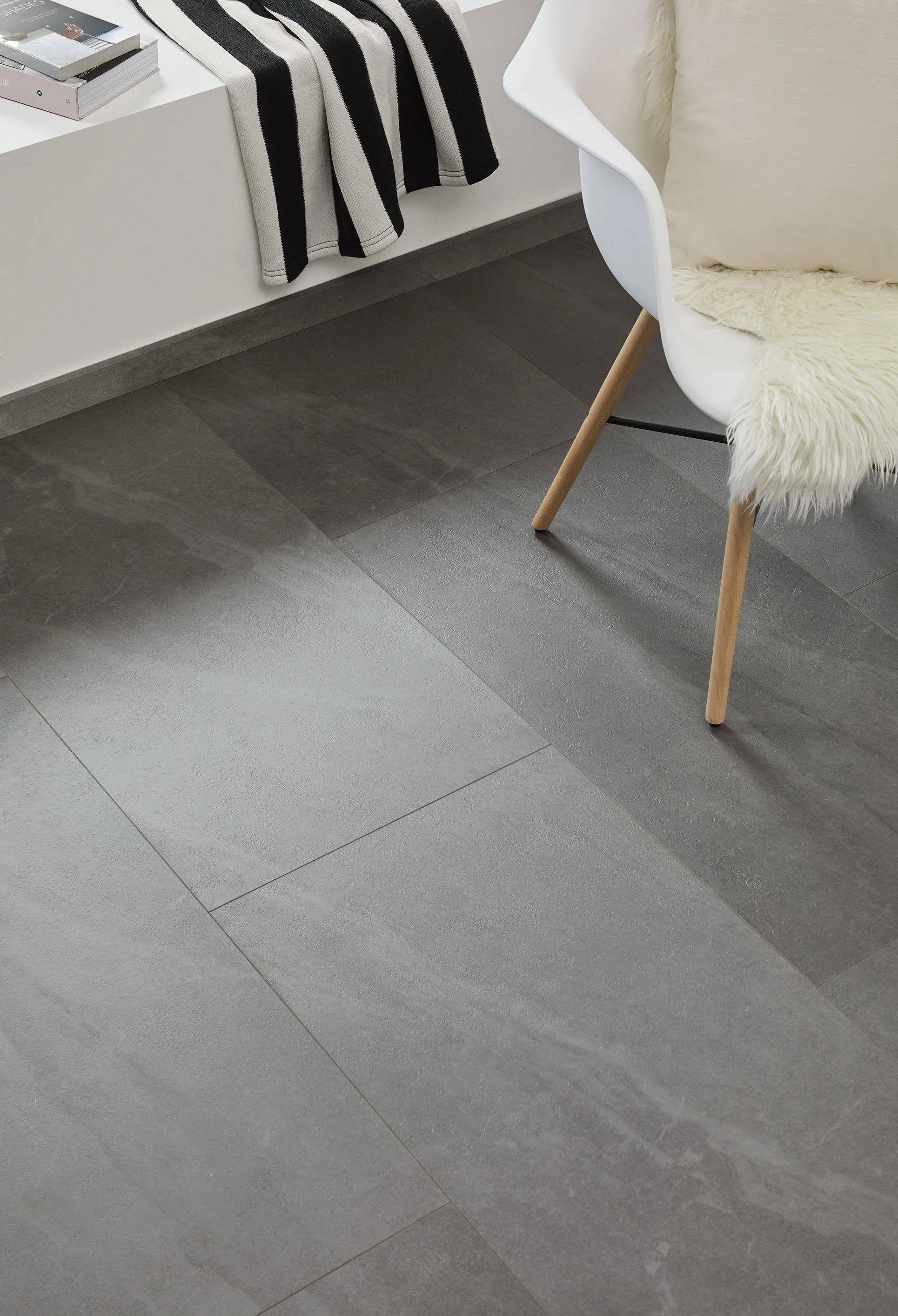 Stone slate effect flooring tiles under a bed and chair. The bed and chair are white and the slate is a dark grey.