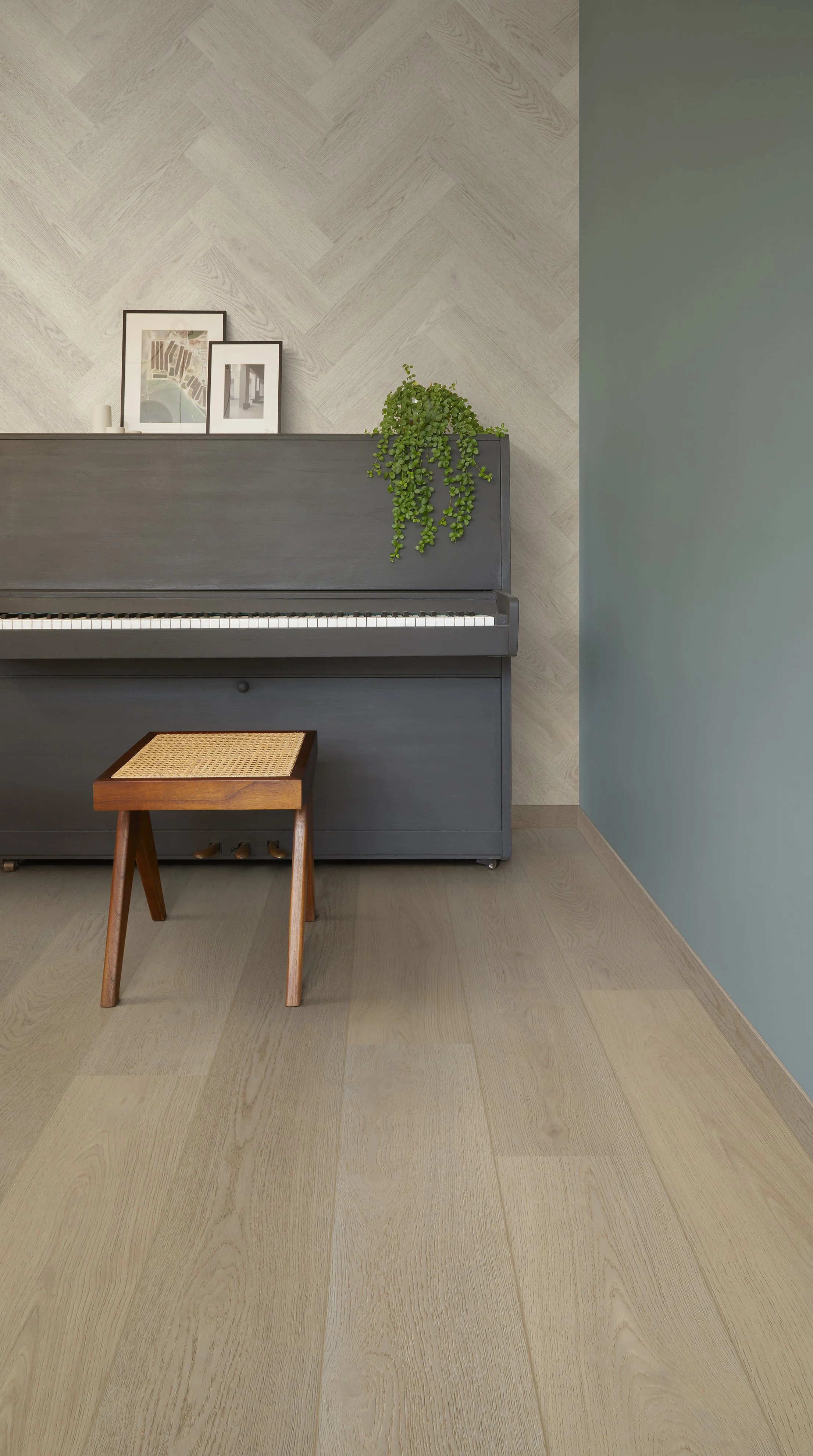 Conrer of a room with a soft light oak wood effect flooring, a painted green wall and a grey modern piano with a stool in front. Gives a minimalist warm contemporary style.