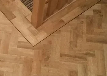 Close-up of a wooden parquet floor in a room corner with a wooden table leg.