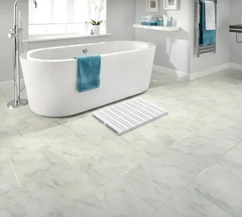 Modern white bathroom with freestanding bathtub, teal towel, striped bath mat, and light-colored marble floor.