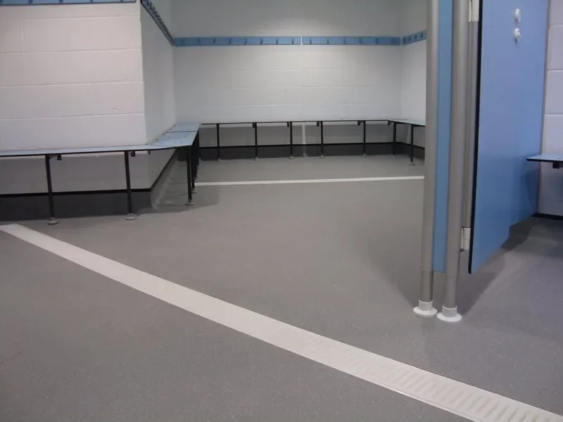 Empty locker room with benches and hooks for clothes, with gray flooring and white and blue walls.