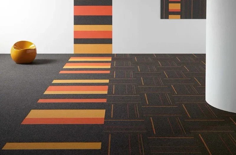 Interior space with carpet featuring geometric patterns in orange and yellow on a black background, curved white wall, and a yellow decorative bowl on the floor.