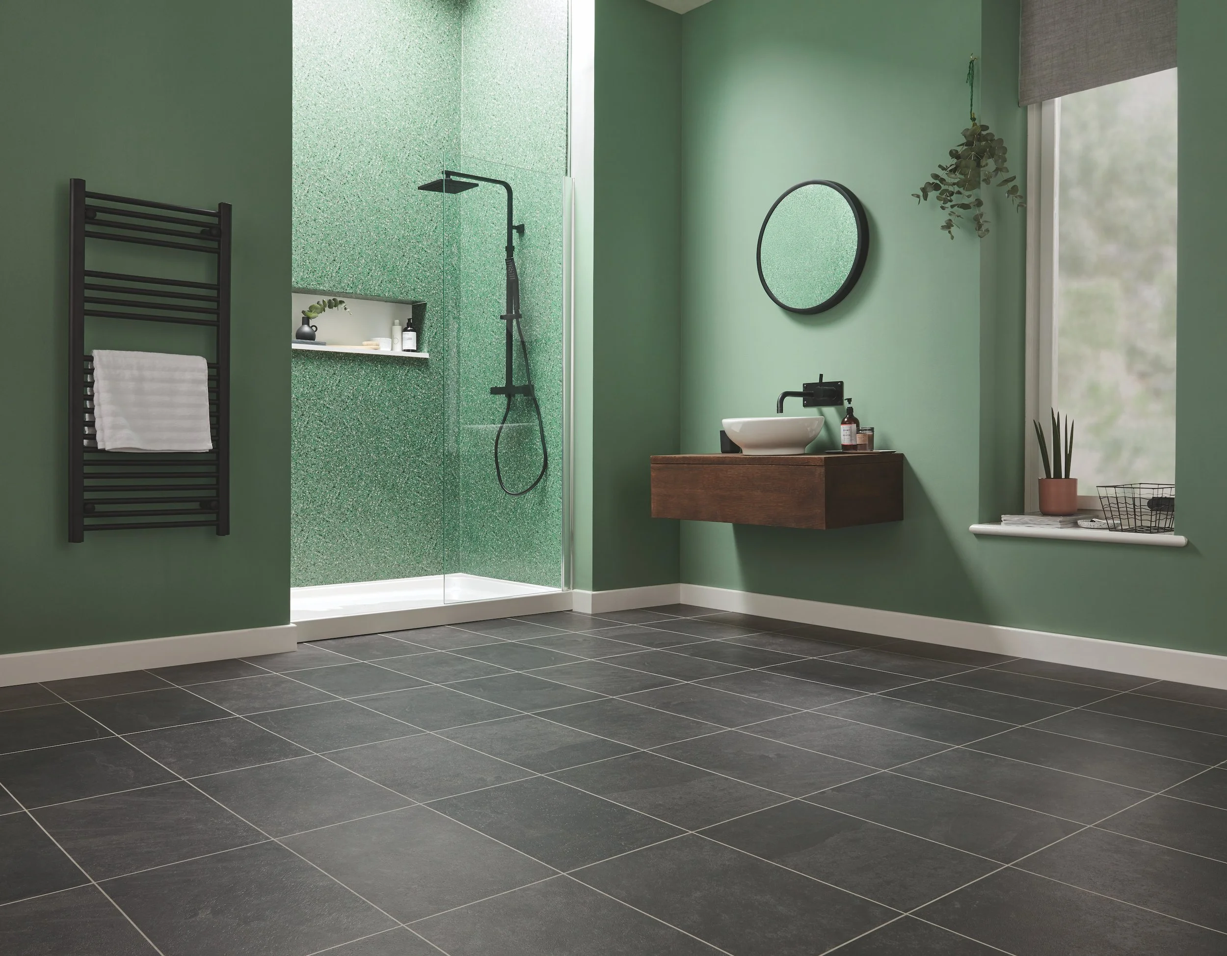 A bathroom with mint green walls, black fittings and a large expanse of dark slate tile effect flooring with pale grout lines in between.