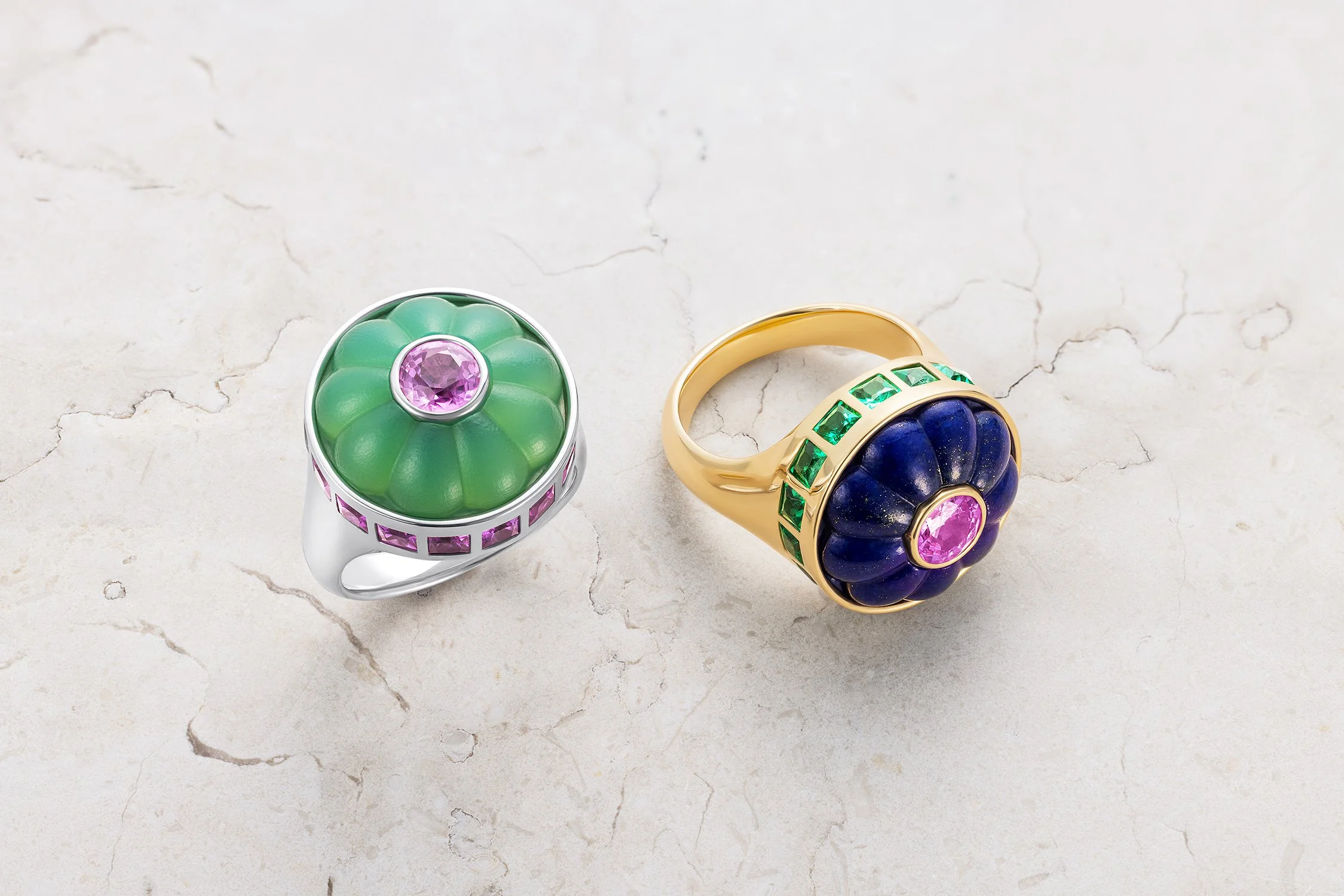 Two colorful rings with gemstone accents on a marble surface.