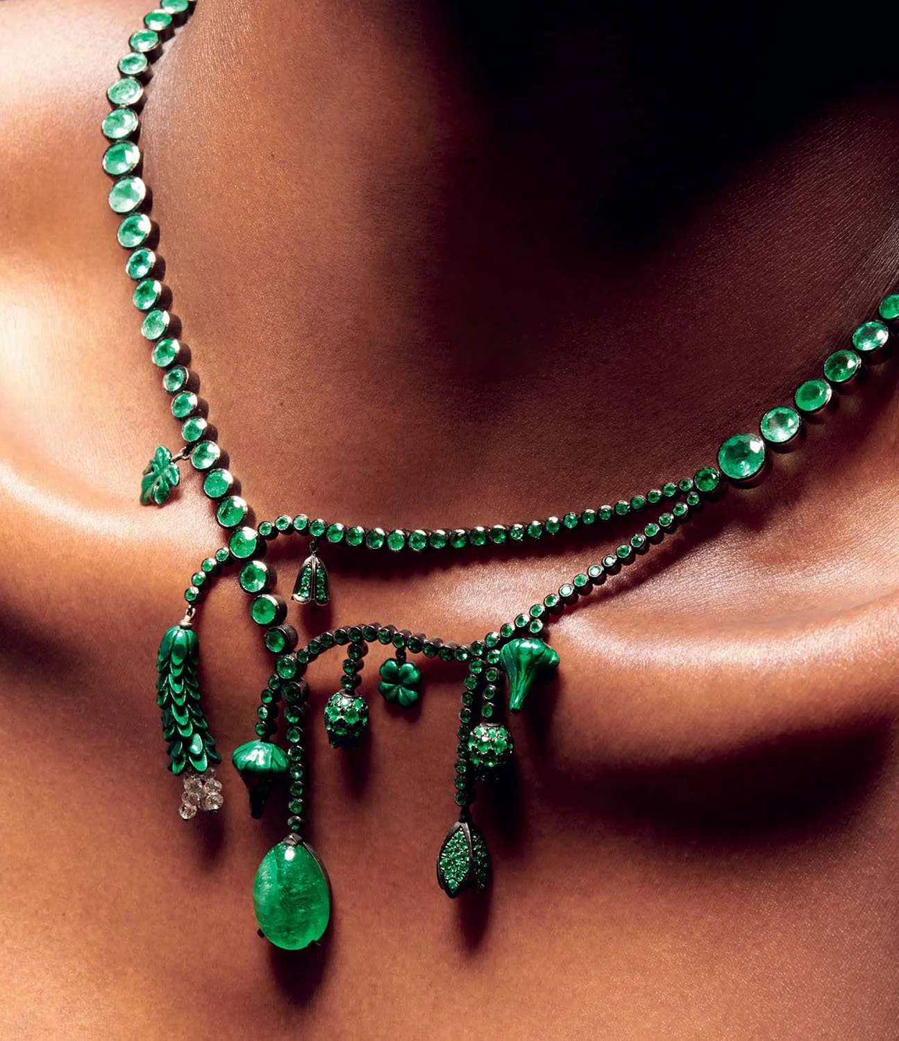 Close-up of a person's neck and collarbone wearing layered green gemstone necklaces with various charms and pendants.