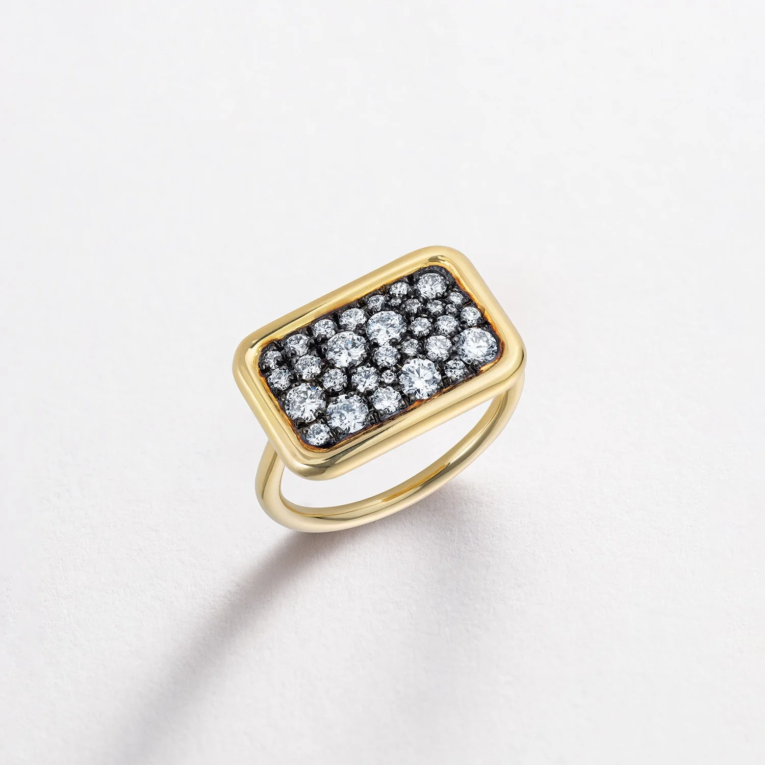 Gold ring with a rectangular face encrusted with multiple small diamonds on a white surface.