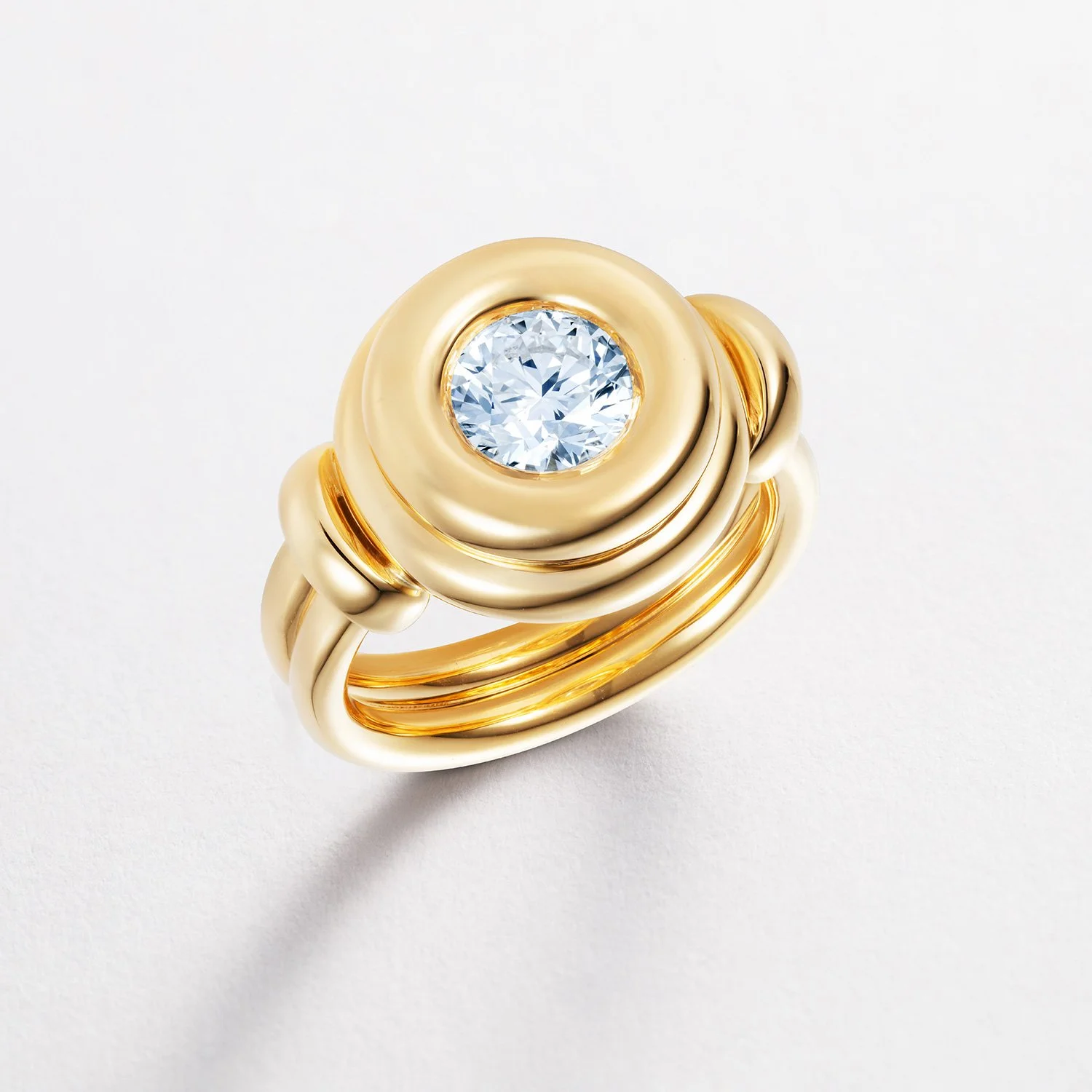 Close-up of a gold ring with a large, round diamond set in the center, resting on a pure white background.