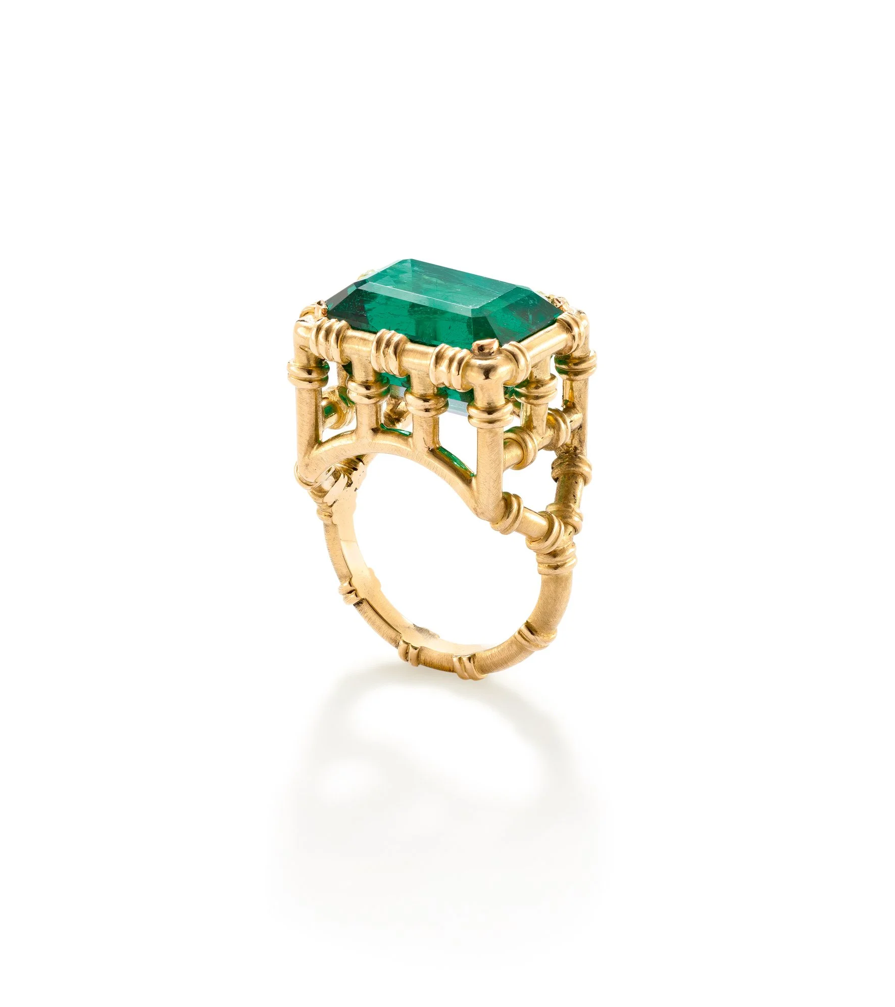 Close-up of a ring with a large green rectangular gemstone set in a gold band with decorative details, on a white background.