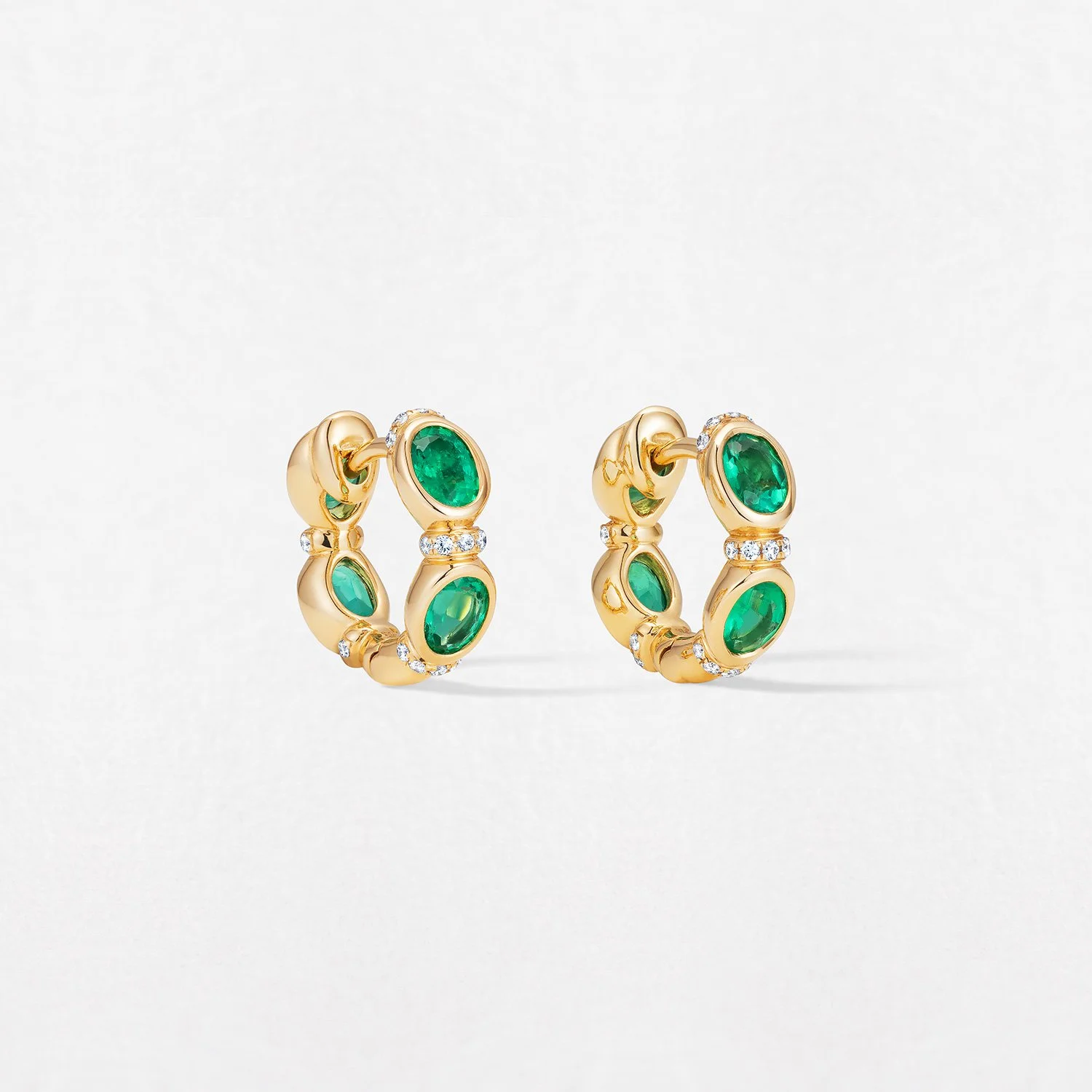 Gold hoop earrings with green gemstones and small diamonds against a white background.