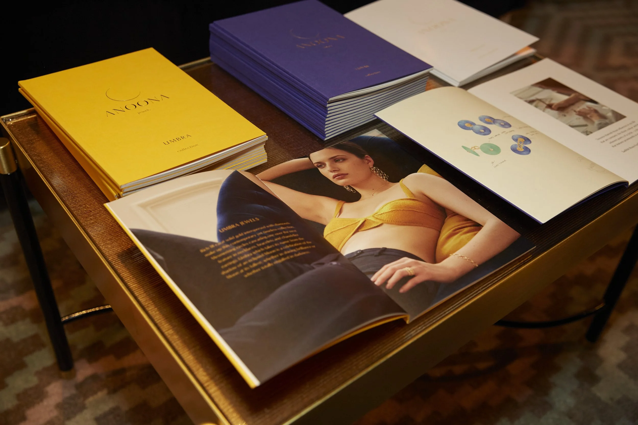 Open magazines on a wooden table, showing fashion photos and colorful designs, with a woman wearing a yellow top in one photo.