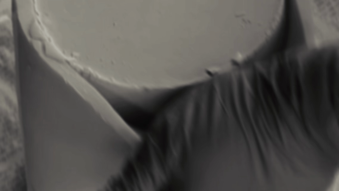 Close-up of a person wearing black gloves handling large, round gray objects, possibly cups or containers, on a textured surface.