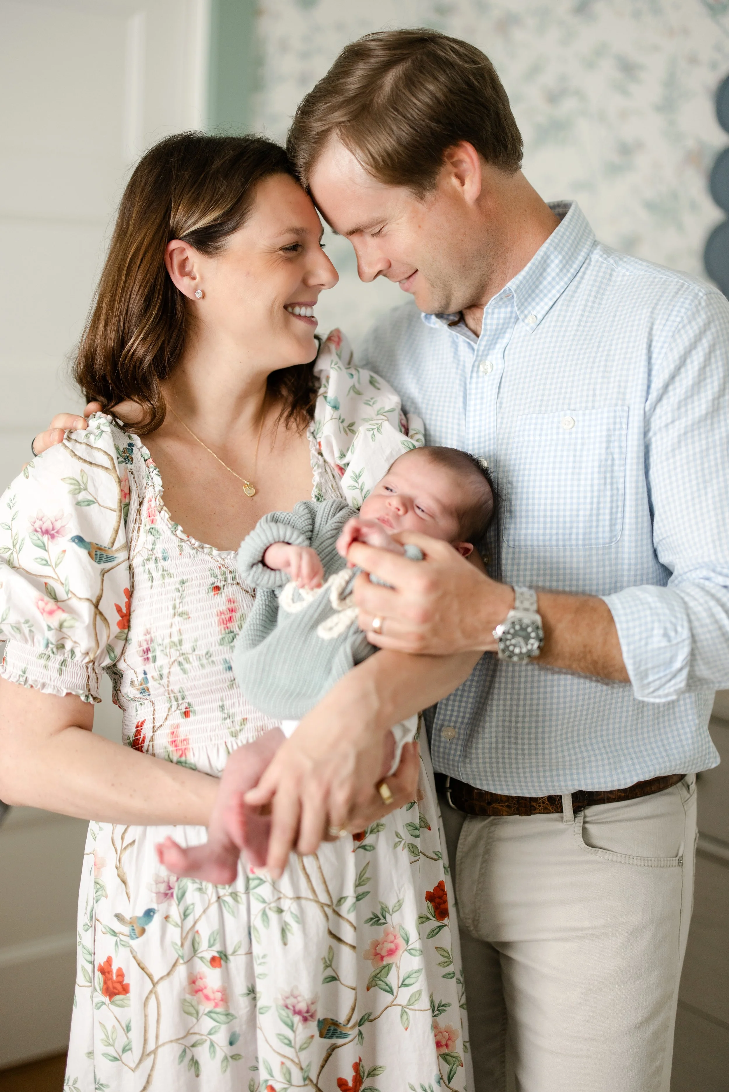 A couple holding a newborn baby in a hospital or home setting, touching foreheads and smiling.