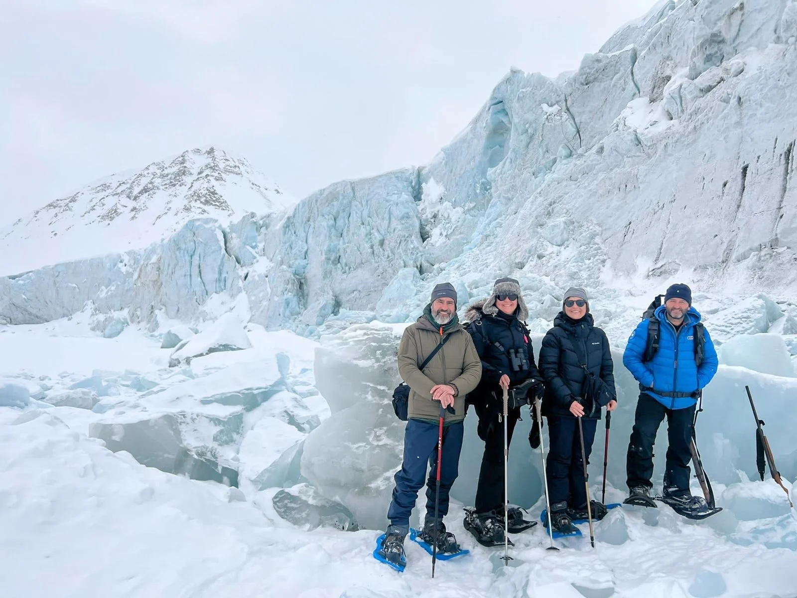 Cuatro personas con ropa de esquí posan frente a un glaciar en la nieve.