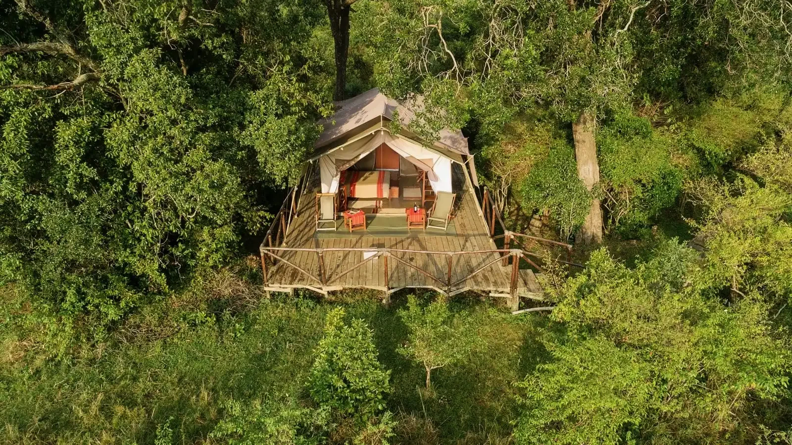 Vista aérea de una cabaña en medio de un bosque, con terraza y muebles de exterior.