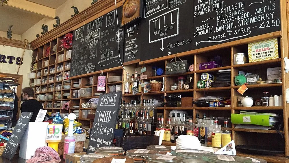 Interior of T H Roberts cafe in Dolgellau with wooden shelves filled with jars, containers, and decorations.