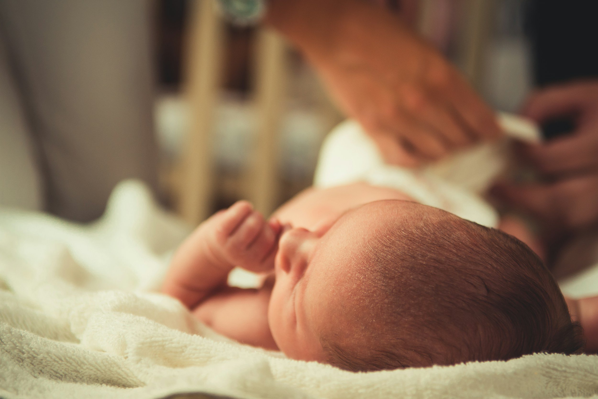 A newborn baby lying on a soft blanket, with a hand gently touching the baby's forehead in a close-up shot.