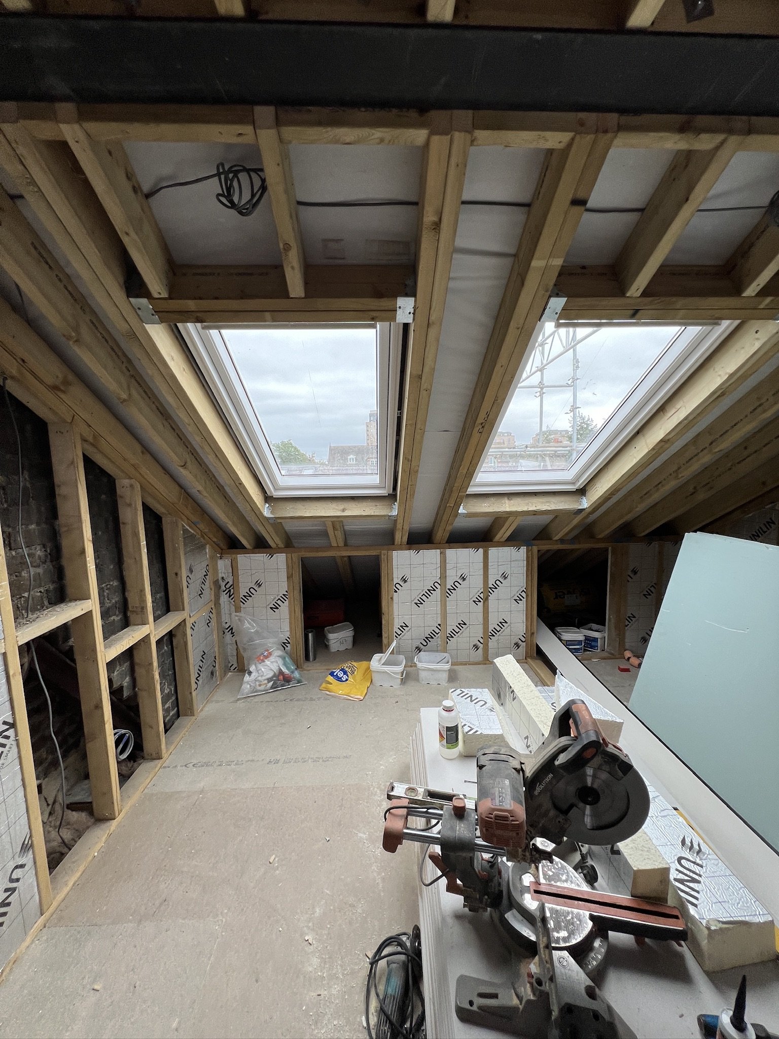 Attic or renovation space with wooden beams, skylights, tools, and construction materials scattered around.