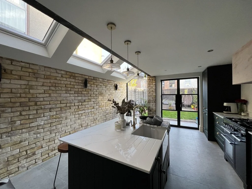 Modern kitchen with brick accent wall, skylights, black cabinetry, and a central island with a white countertop.