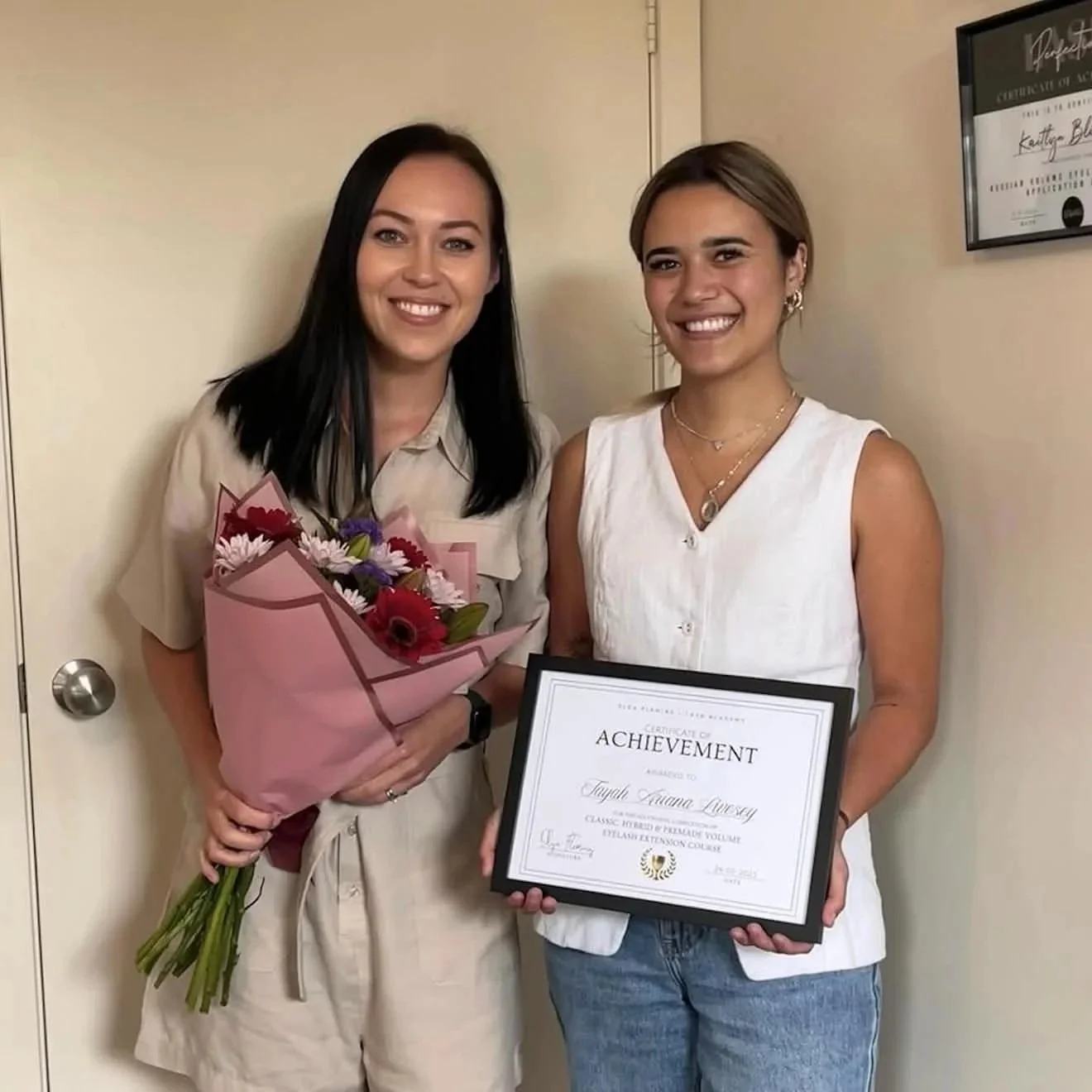 Olga Fleming with lash student Sophie holding flowers and her lash training certificate after completing her course.