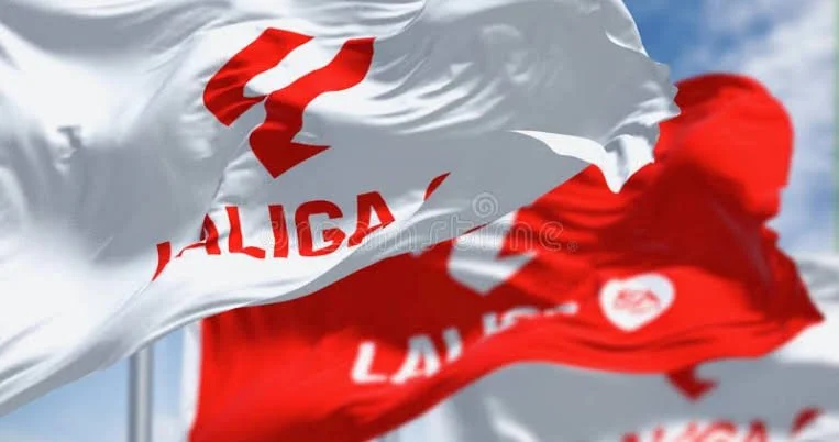 Two flags, one white and one red, waving in the wind, with partially visible text and logos.