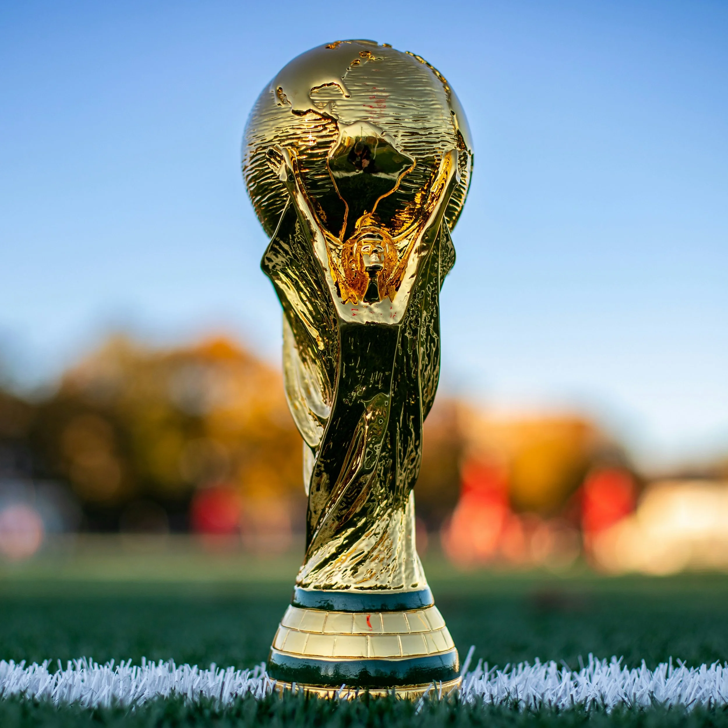 The FIFA World Cup trophy made of gold and silver, placed on a green grass field with a blurred background of colorful lights.