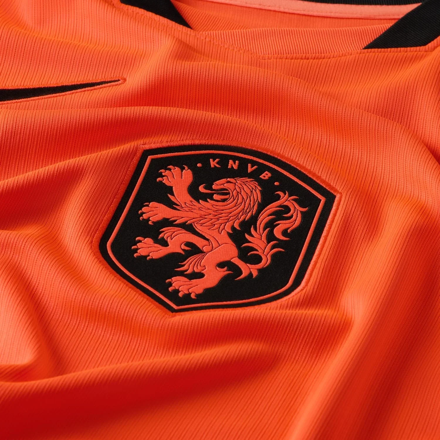 Close-up of an orange sports jersey with a black and orange crest featuring a lion and the text 'KNVB'.