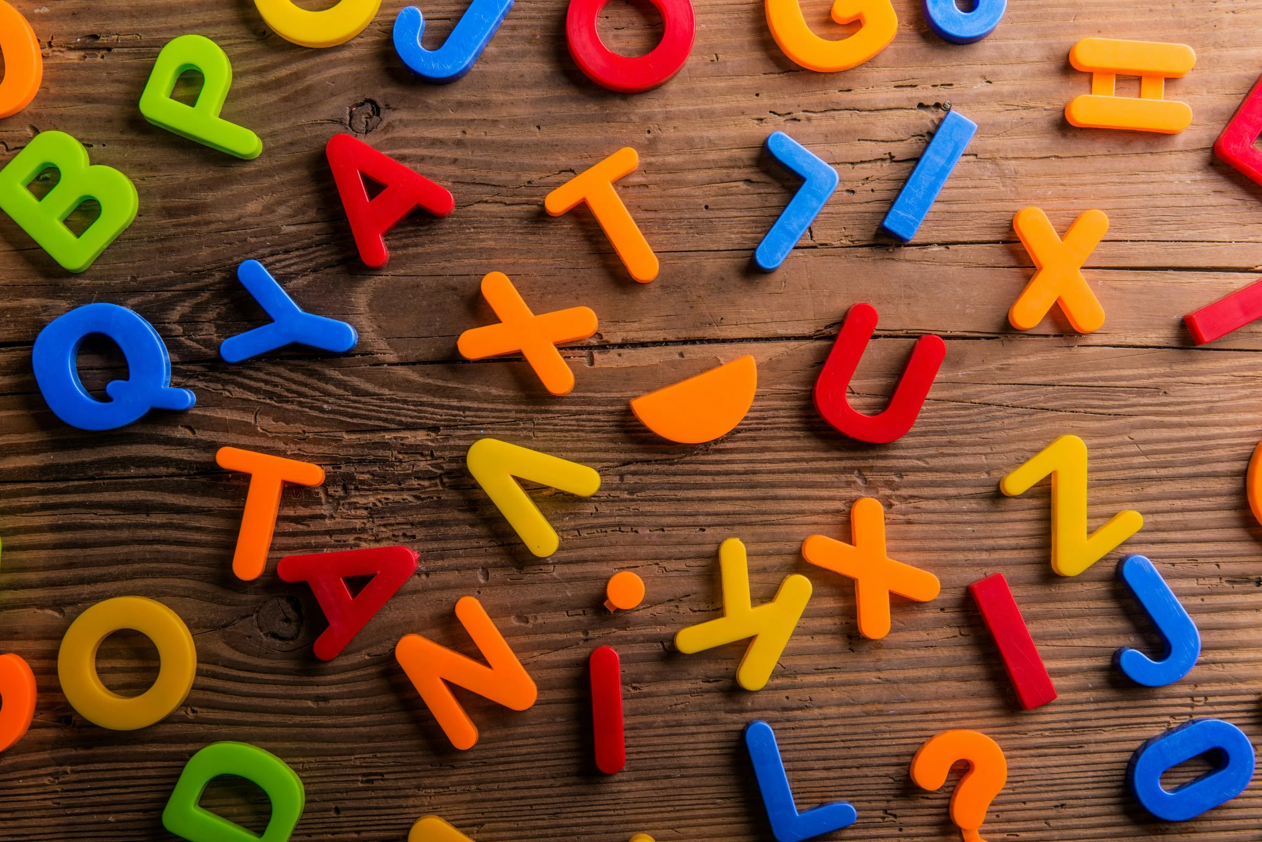 Colorful plastic alphabet letters scattered on a wooden surface.