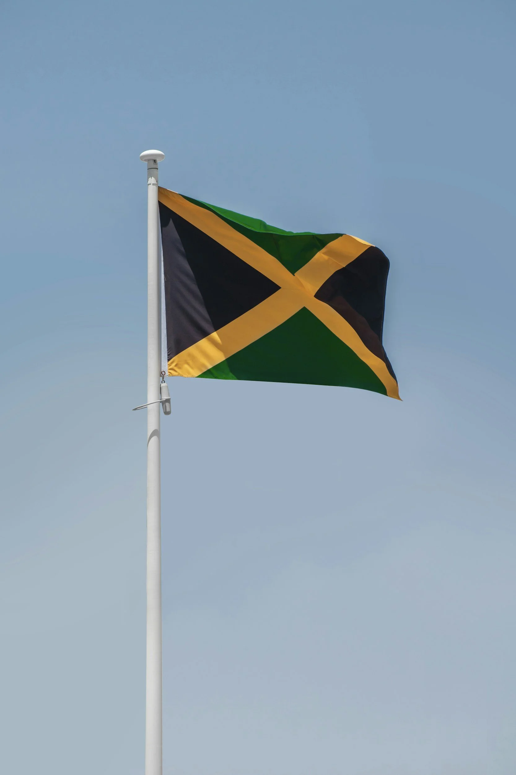 The Jamaican flag flying on a white flagpole against a clear blue sky.
