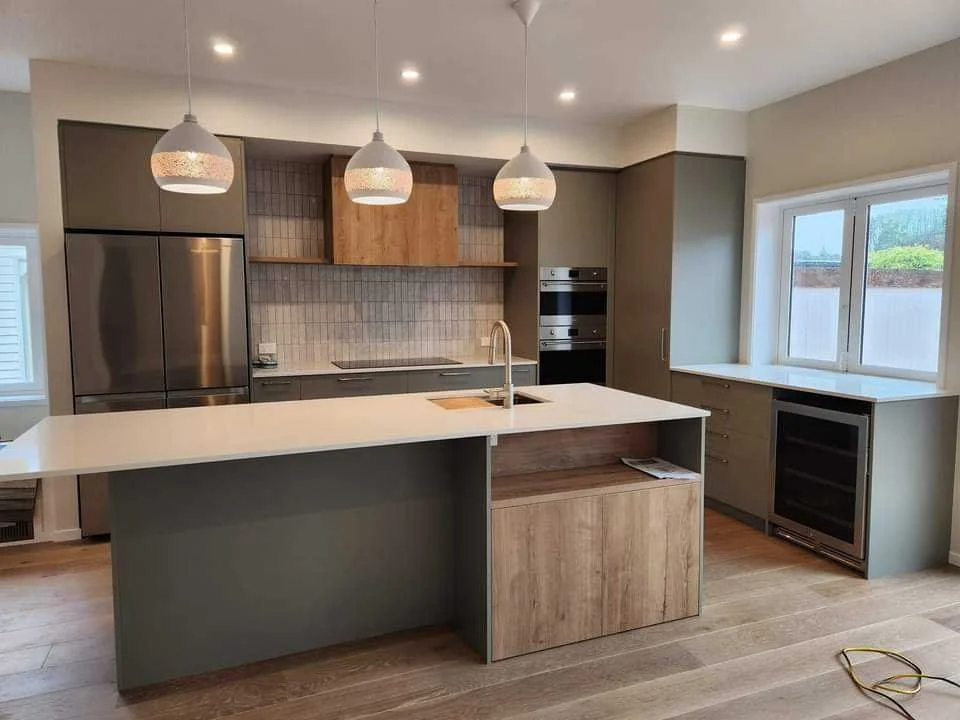 Modern kitchen with a white island counter, gray cabinetry, a built-in oven, stainless steel refrigerator, and pendant lighting.