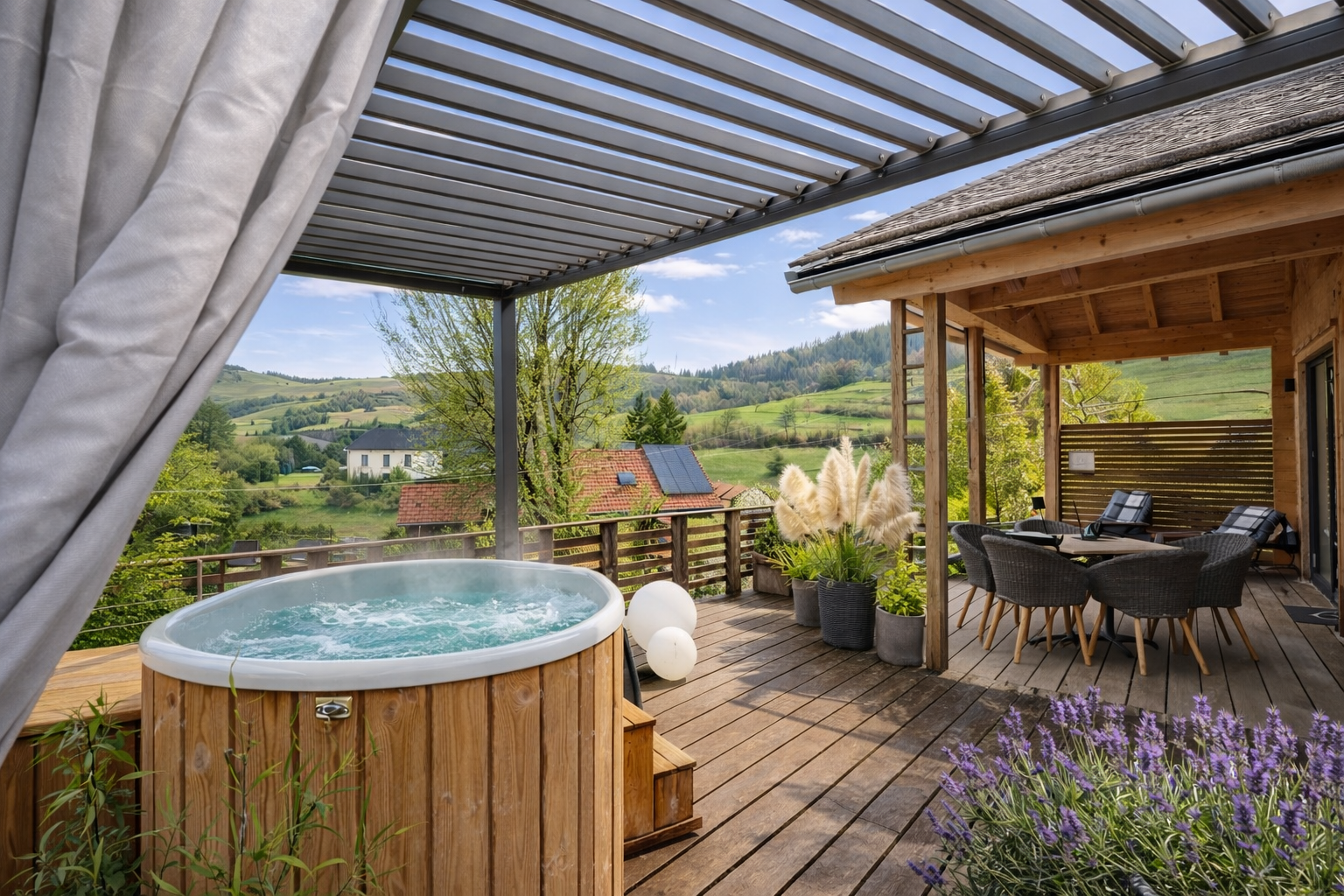 Gemütliche Terrasse mit Whirlpool und Sitzgruppe, umgeben von Pflanzen, mit Blick auf grüne Hügel und Häuser im Hintergrund