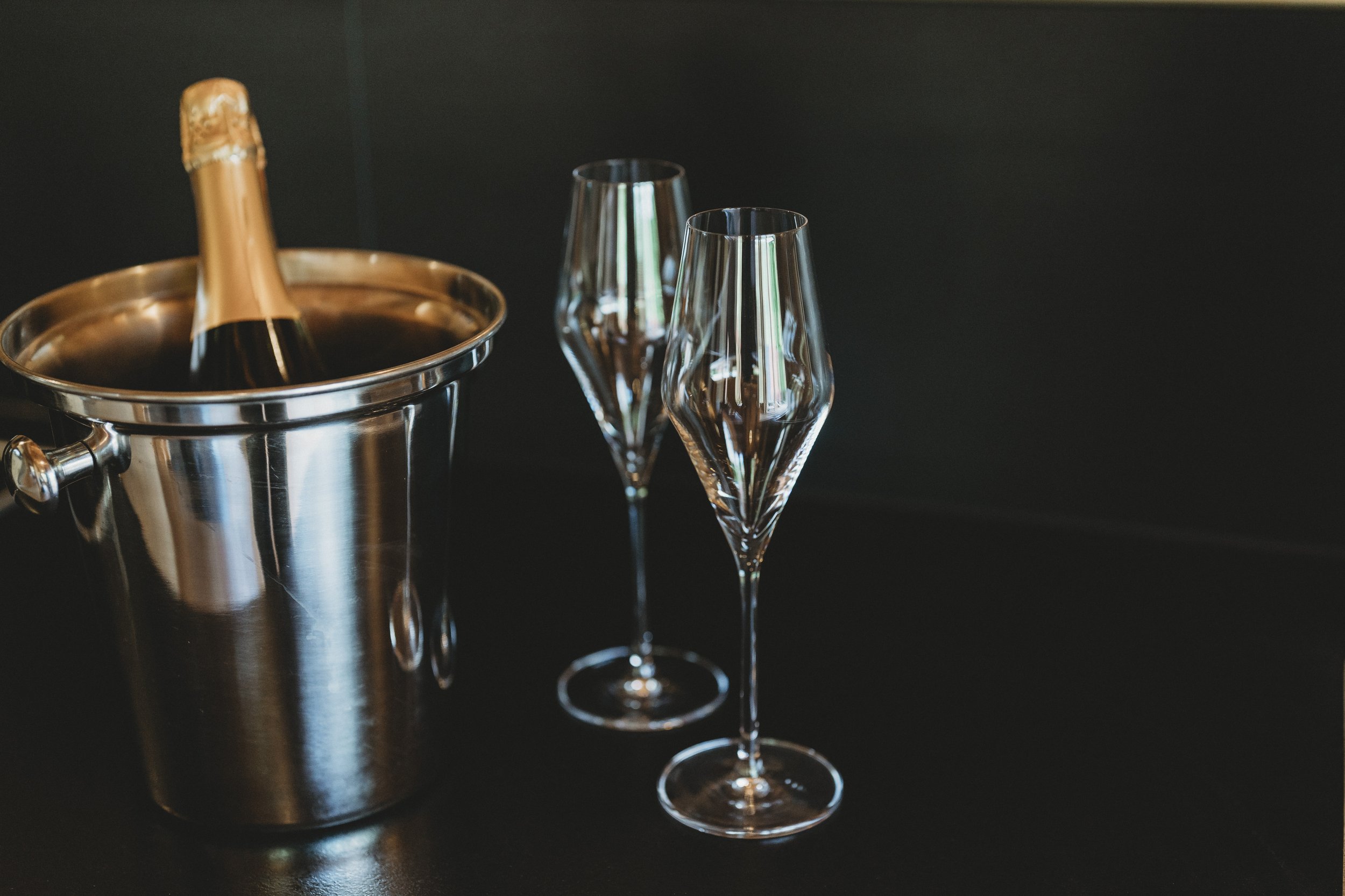 Sektflasche in einem Eiskübel, zwei Champagnergläser auf einem schwarzen Tisch.