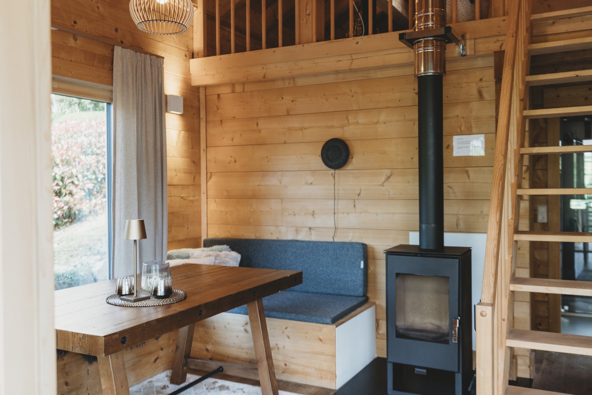 Innenraum eines Holzhauses mit Esstisch, Couch, Kamin und Holztreppe.